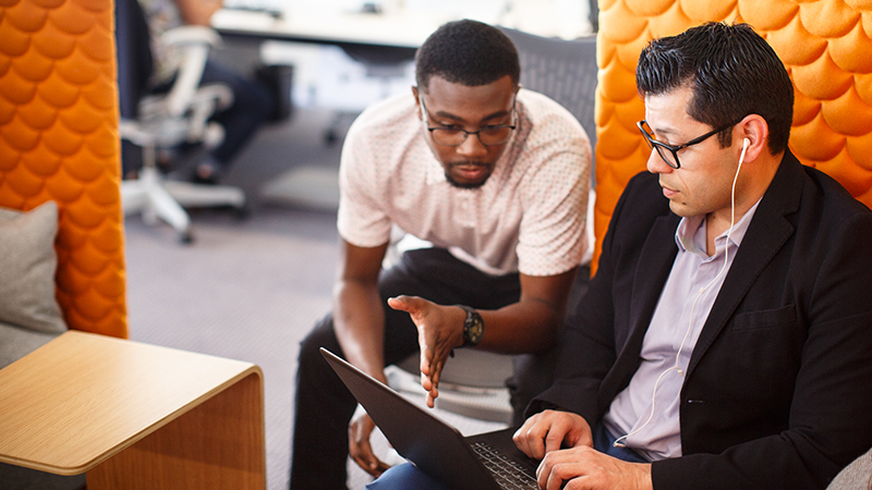 Two people discussing at work Two seated men discussing laptop display.