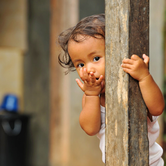 Young baby peering behind a wooden beam 