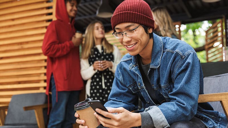 Smiling man with coffee in his hand uses his cell phone